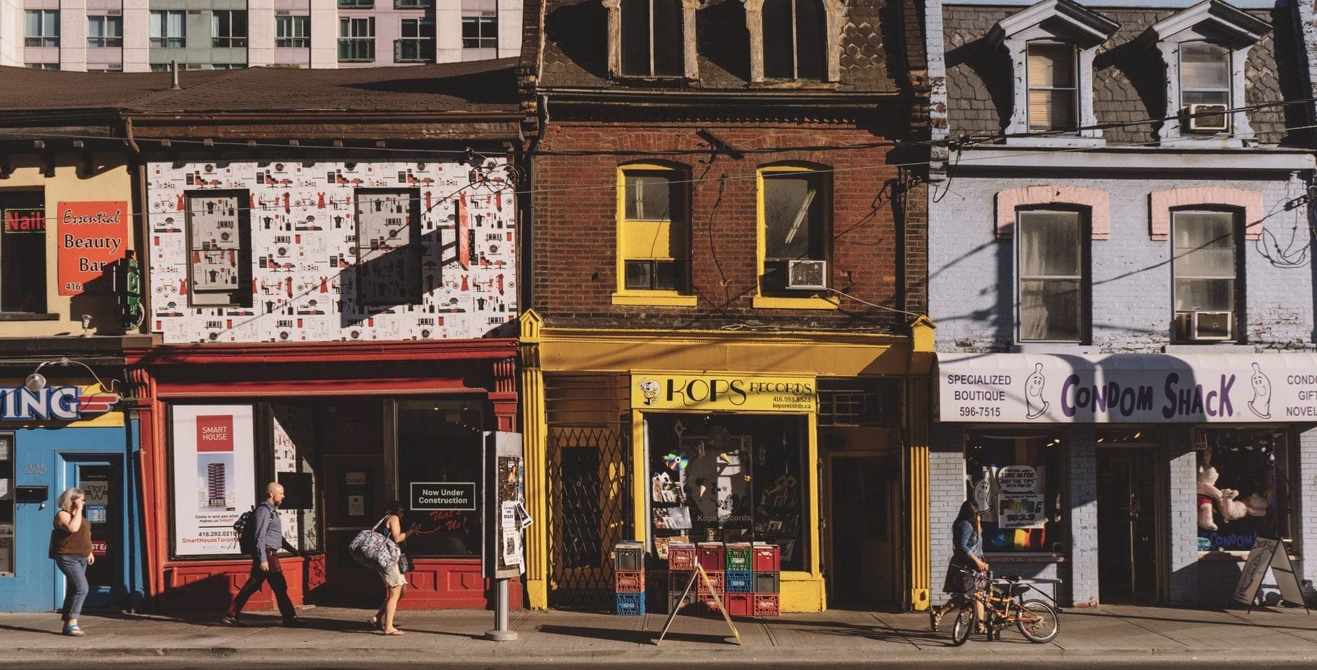Fachadas coloridas con tiendas independientes y peatones caminando por Queen Street West en Toronto en un día soleado.