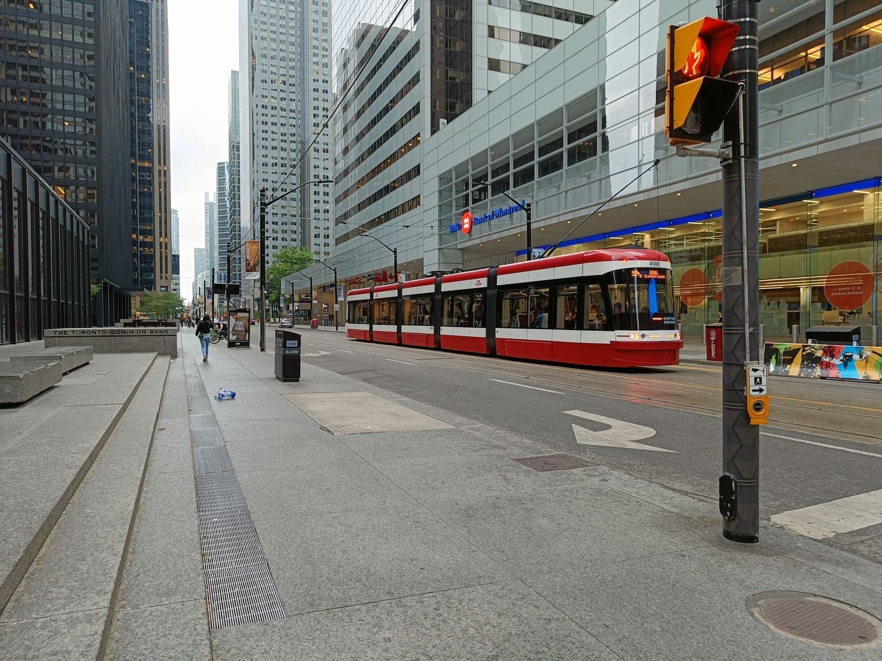 Moderno tram di Toronto rosso e bianco che percorre il centro città con alti edifici di vetro e scena stradale urbana di giorno.