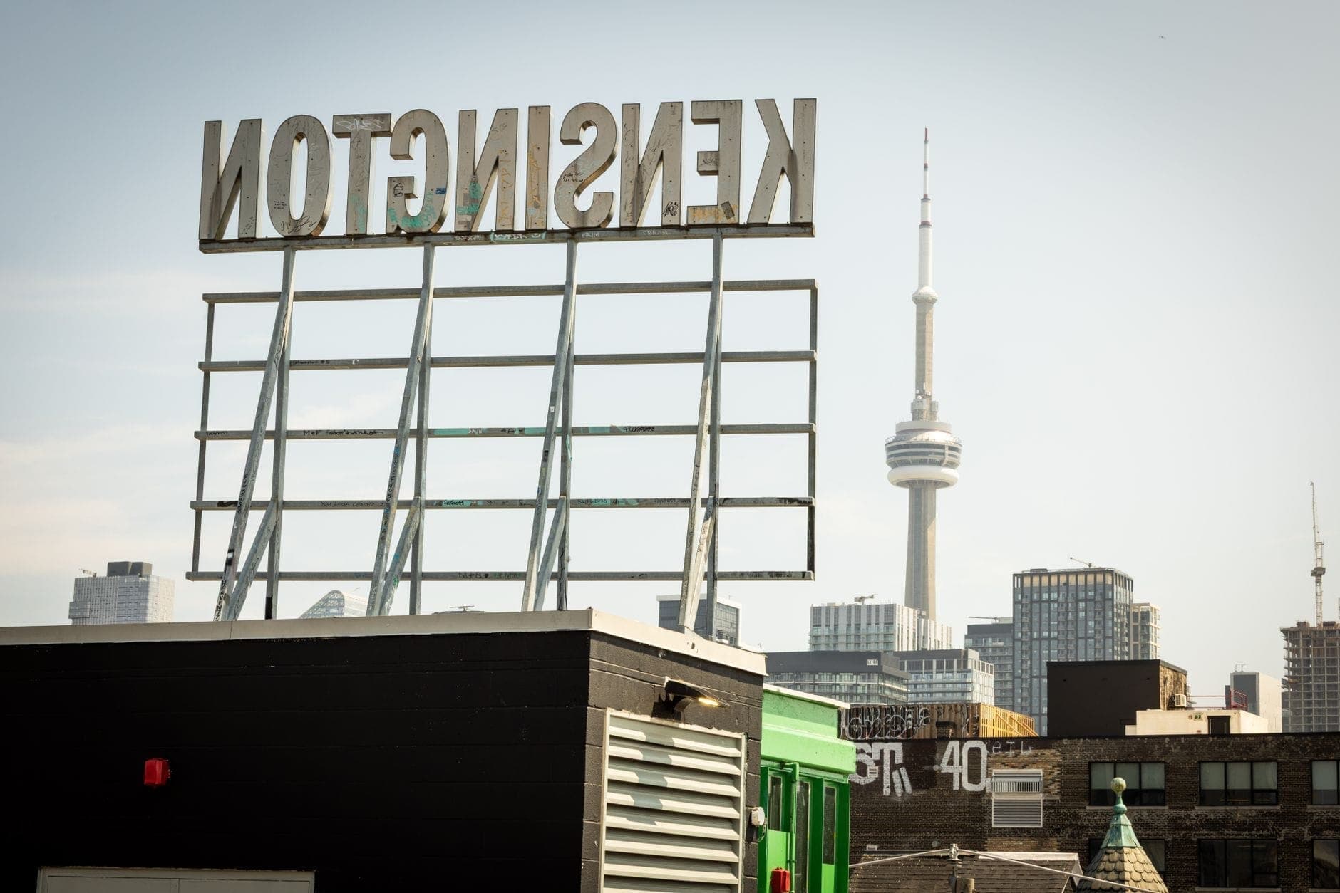 Skyline di Toronto con la CN Tower e l'insegna di Kensington in primo piano, che cattura un notevole quartiere del centro per i viaggiatori solitari.