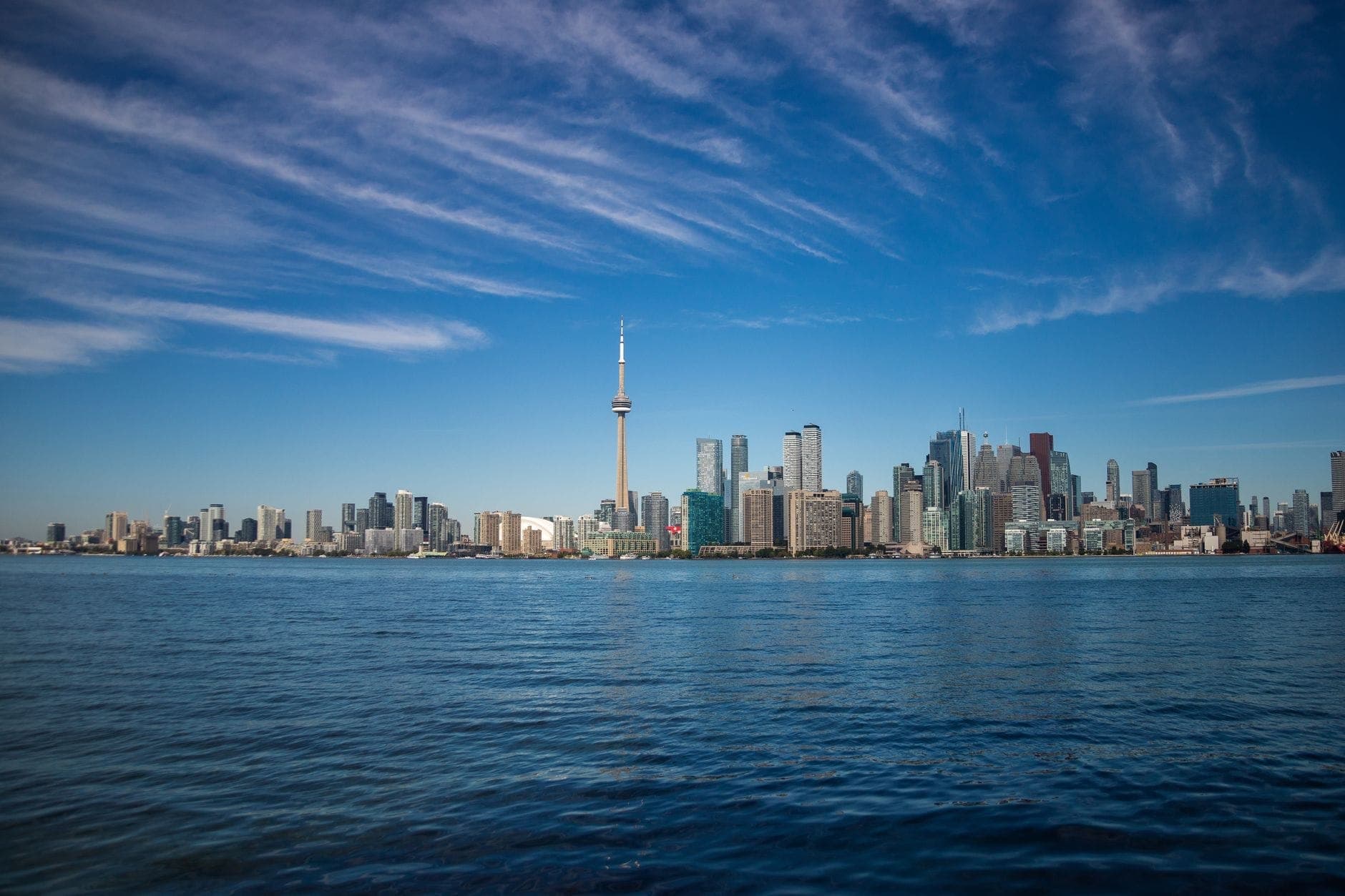 Pemandangan luas cakrawala tepi danau Toronto di hari cerah dengan langit biru dan air danau yang tenang di latar depan.