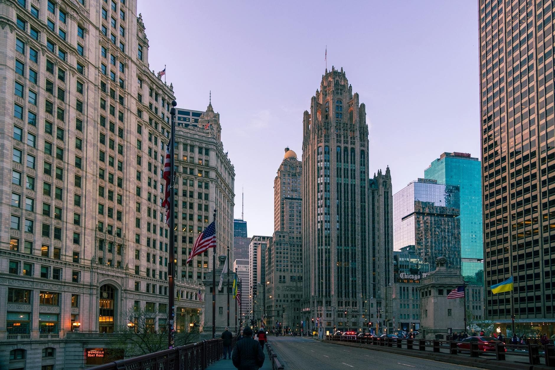 A view down Michigan Avenue at dusk with the Tribune Tower’s neo-Gothic spire rising centrally, surrounded by iconic Chicago skyscrapers in a vibrant urban streetscape.
