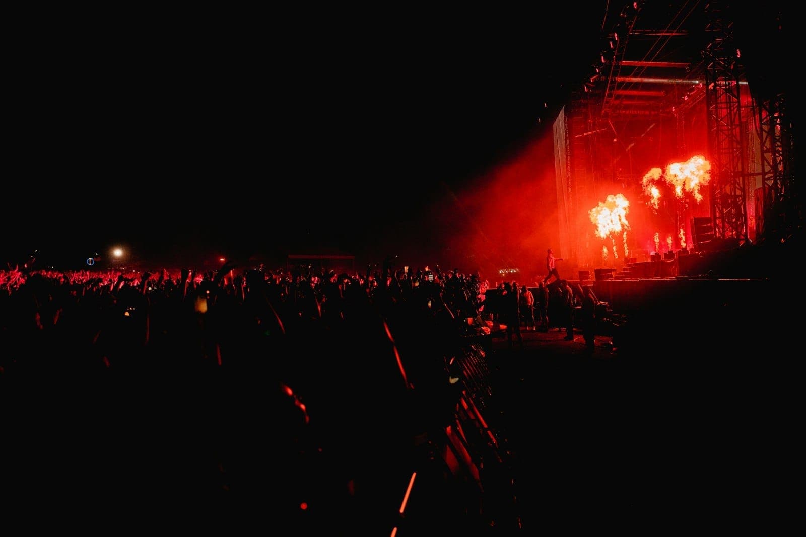 Una folla enorme a un festival musicale notturno, con luci rosse accecanti sul palco e fuochi pirotecnici che trasmettono tutta l'energia di un evento all'aperto.