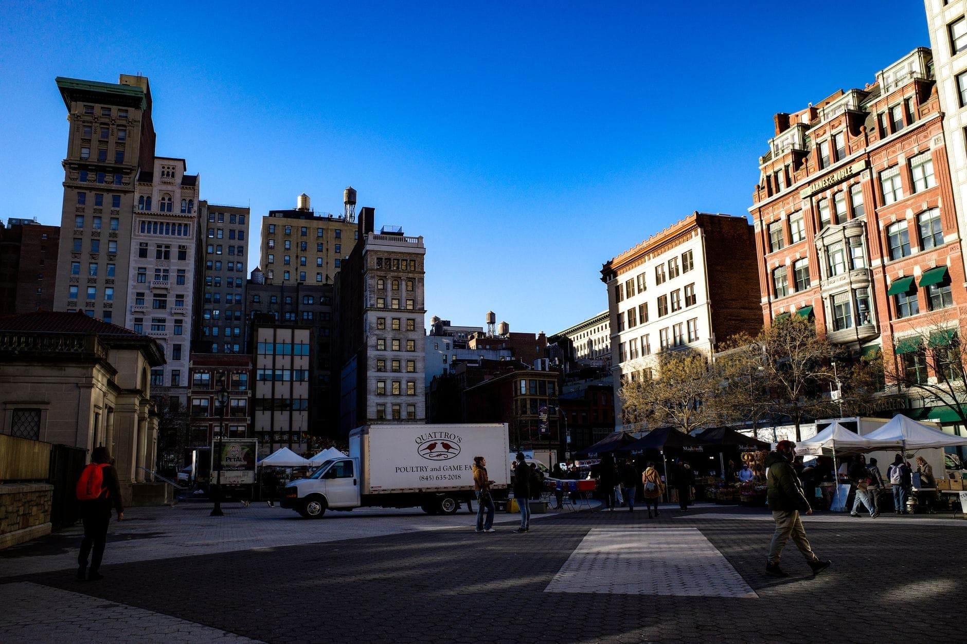 ภาพตลาด Union Square Greenmarket เต็นท์ขาวเรียงราย รถตลาด คนเดินช้อปในลานกว้าง รายล้อมด้วยตึกแมนฮัตตัน ใต้ท้องฟ้าสีฟ้าใส