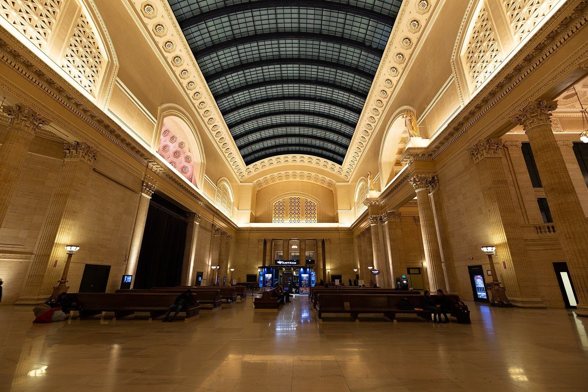 Wide-angle view of the Union Station Great Hall in Chicago, featuring tall marble columns, benches, and a soaring glass barrel-vaulted skylight.