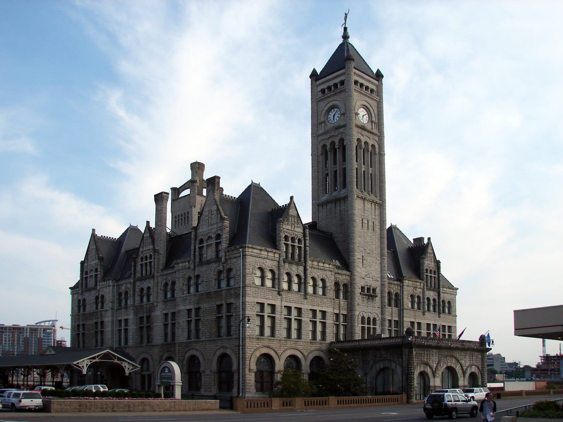 Union Station Hotel Nashville features a striking Gothic Revival facade with a tall clock tower, limestone walls, and arched windows under a blue sky.