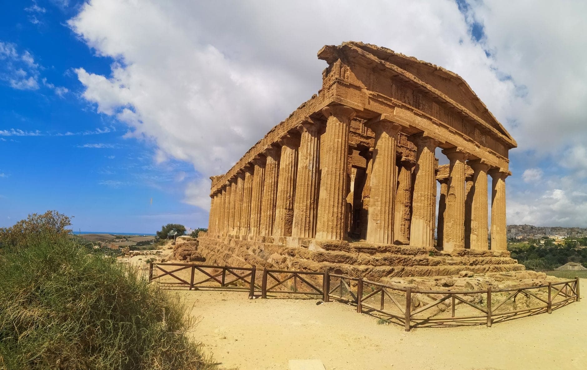 Pemandangan panorama Kuil Concordia kuno bergaya Yunani yang terawat baik di bawah langit biru cerah dengan awan berpencar di Lembah Kuil, Agrigento.