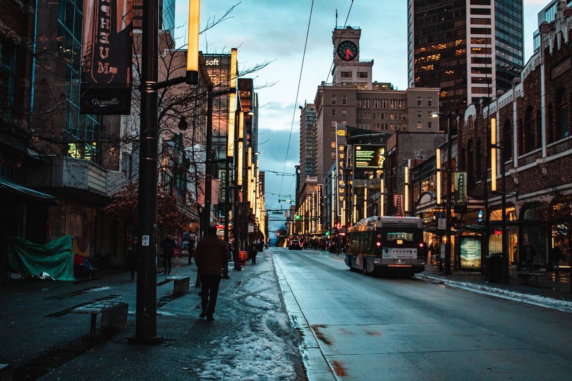 Granville Street ในใจกลางเมืองแวนคูเวอร์ยามพลบค่ำ พร้อมแสงไฟนีออน ผู้คน และรถบัส สะท้อนบรรยากาศย่านบันเทิงของเมือง