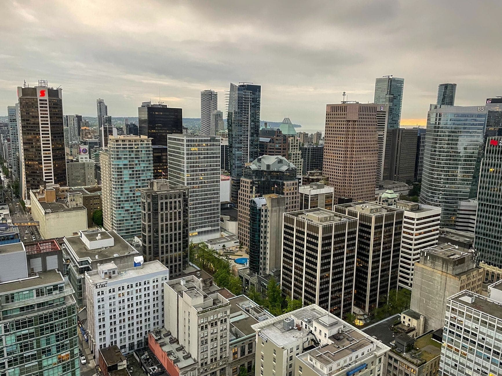 ภาพมุมสูงของใจกลางเมือง Vancouver ที่เต็มไปด้วยตึกระฟ้าและช่วงตึกต่างๆ ใต้ท้องฟ้าที่มีเมฆปกคลุม
