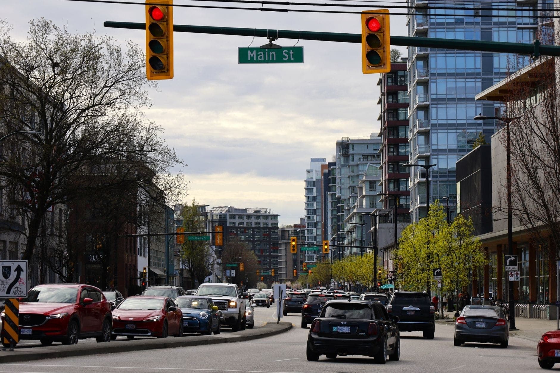 วิวถนน Main Street ในเมือง Vancouver พร้อมรถยนต์ อาคารสมัยใหม่ และป้ายชื่อถนนที่มองเห็นได้ด้านบน