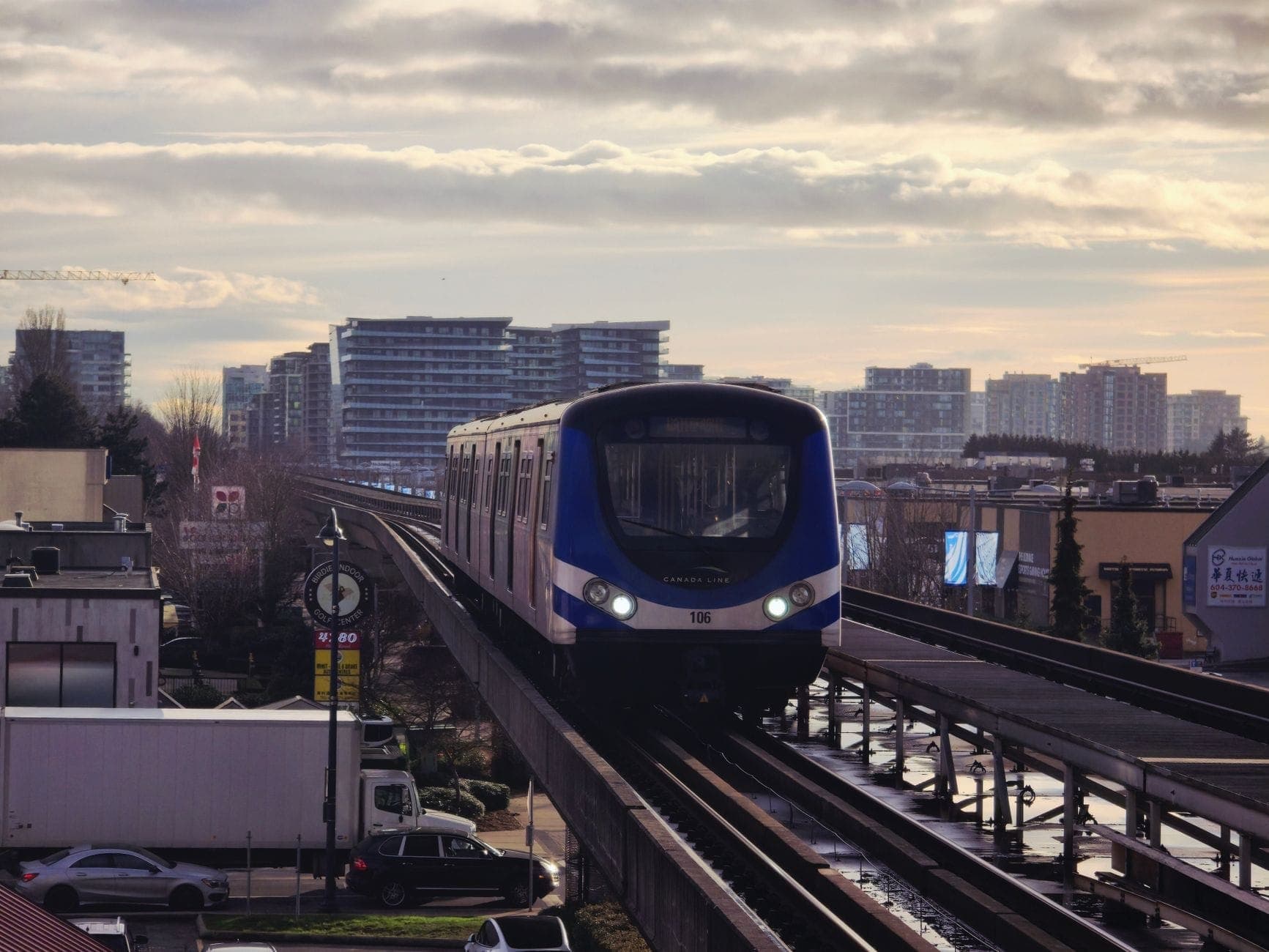 รถไฟ Canada Line SkyTrain วิ่งบนรางยกระดับผ่านเมือง Richmond โดยมีอาคารในเมืองเป็นฉากหลังใต้ท้องฟ้ามีเมฆ