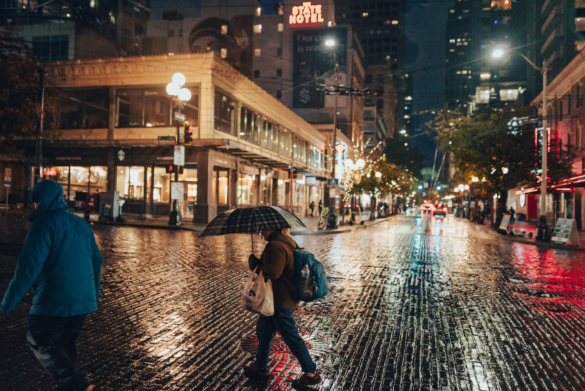 ฉากถนนยามเย็นในวันฝนตกใจกลางเมือง Vancouver มีผู้คนเดินใต้ร่ม และเงาสะท้อนบนพื้นถนนที่เปียกชื้น