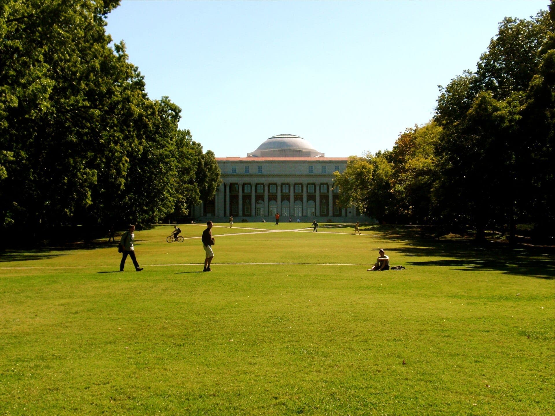 Wide lawn at Vanderbilt University campus with people walking and biking under sunny skies, framed by large trees and a domed historic building.