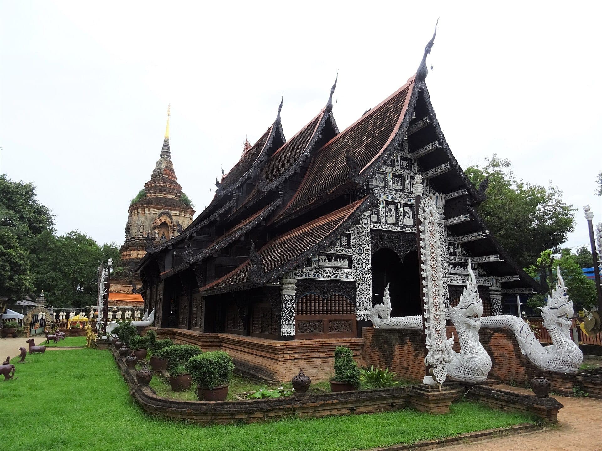 Wat Lok Moli Tempel in Chiang Mai mit aufwendiger Holzarchitektur, weißen Naga-Skulpturen am Eingang und einem alten Backstein-Chedi im Hintergrund.