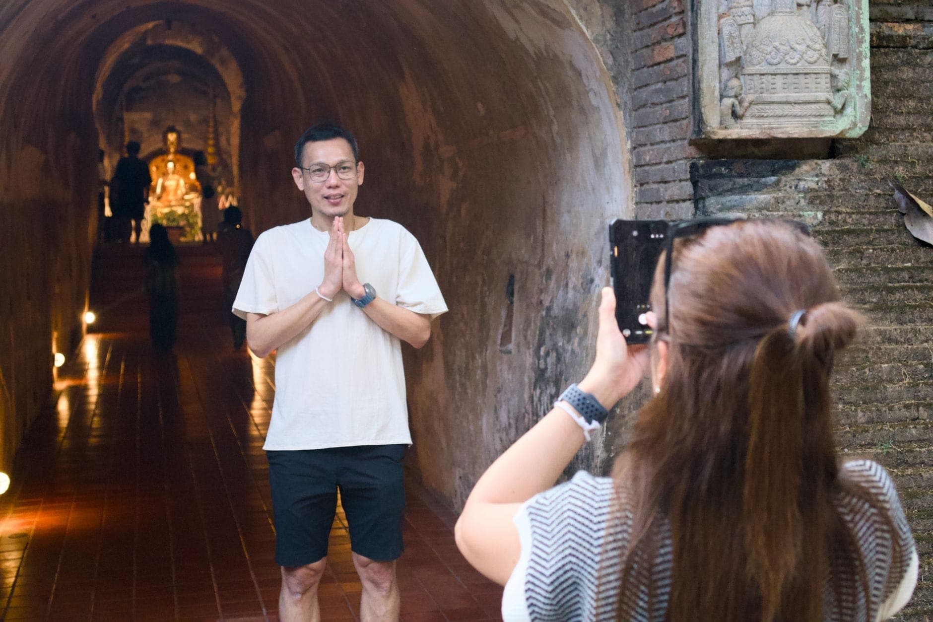 Zwei Menschen in den alten Backsteintunnel von Wat Umong – eine Person fotografiert die andere in der Nähe einer Buddha-Statue am Ende des Tunnels.