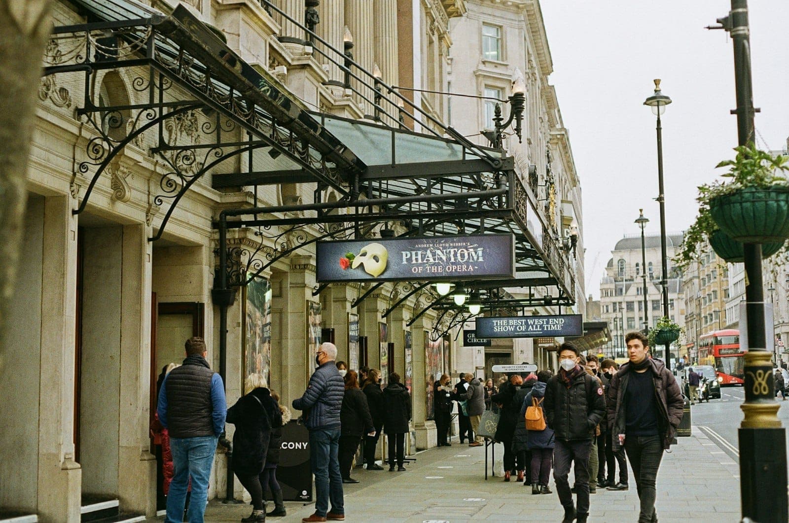 Des passants déambulent dans une rue animée du West End, bordée de théâtres historiques dont les enseignes du Fantôme de l'Opéra, illustration parfaite de l'atmosphère électrique du quartier des théâtres londoniens.