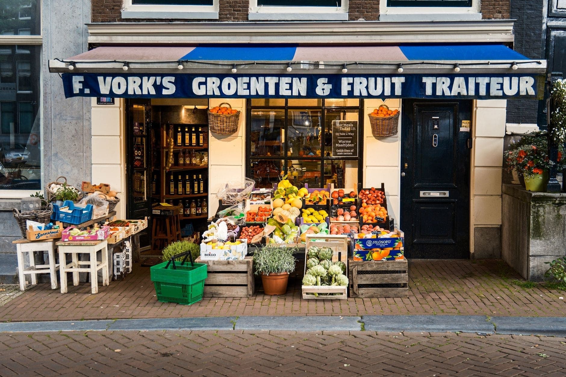 Traditionelle Ladenfront in Amsterdam mit dem Schild 'Groenten & Fruit Traiteur' und frischen Produkten auf dem Bürgersteig.