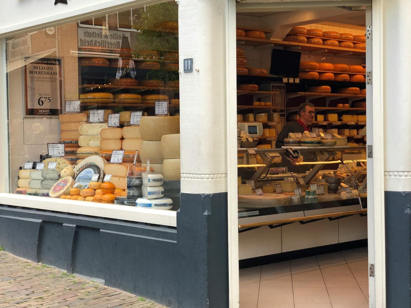Blick in einen traditionellen holländischen Käseladen in Amsterdam mit Regalen voller runder Käselaibe und einer Person hinter der Theke.