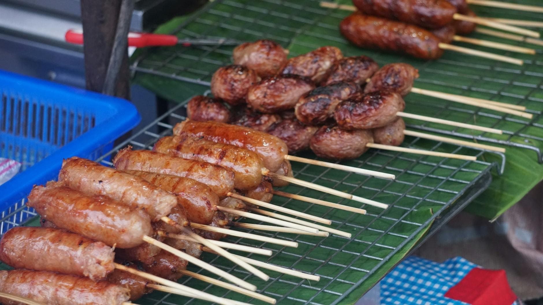 Gegrillte nordthailändische Würste und andere Fleischspieße auf einem traditionellen Streetfood-Grill an einem Marktstand in Chiang Mai.