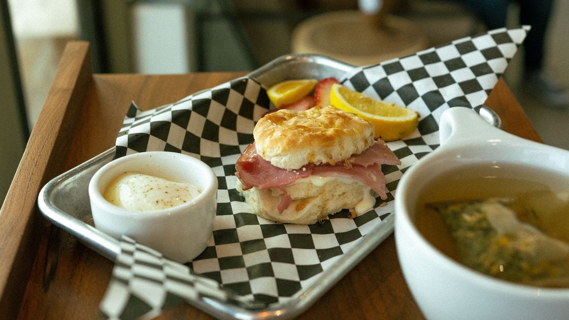 Sándwich de galleta con jamón, rodajas de fruta y una pequeña taza de salsa en una bandeja de un café de desayuno.