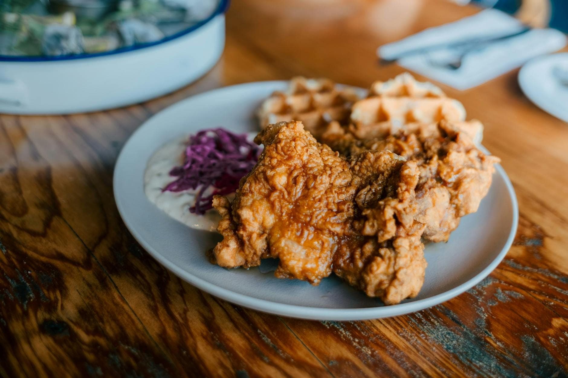 Close-up of a plate of crispy fried chicken and golden waffles served with creamy slaw and gravy, classic Southern comfort food on a rustic wooden table.