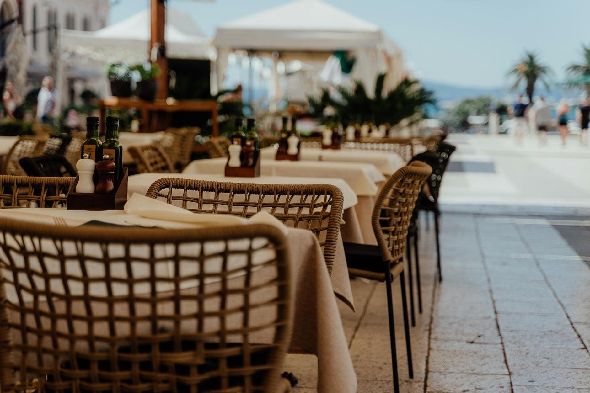 Tavoli di un ristorante all'aperto sul lungomare di Spalato con olio d'oliva e spezie, atmosfera accogliente con palme e vista sull'Adriatico sullo sfondo.