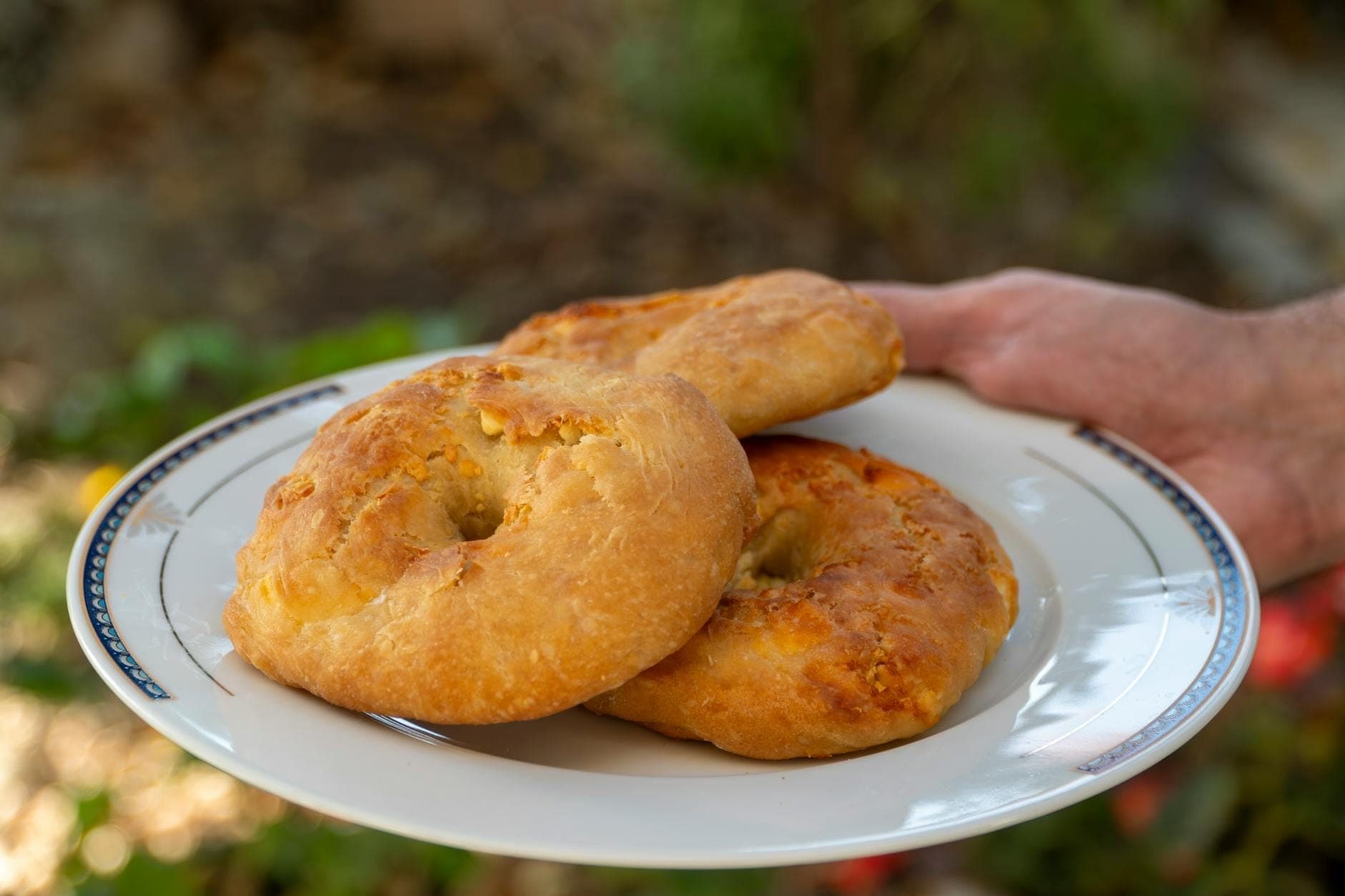 Trois pains plats ronds et rustiques à la croûte dorée servis sur une assiette blanche, tenus en extérieur, représentant le pain traditionnel dalmate.