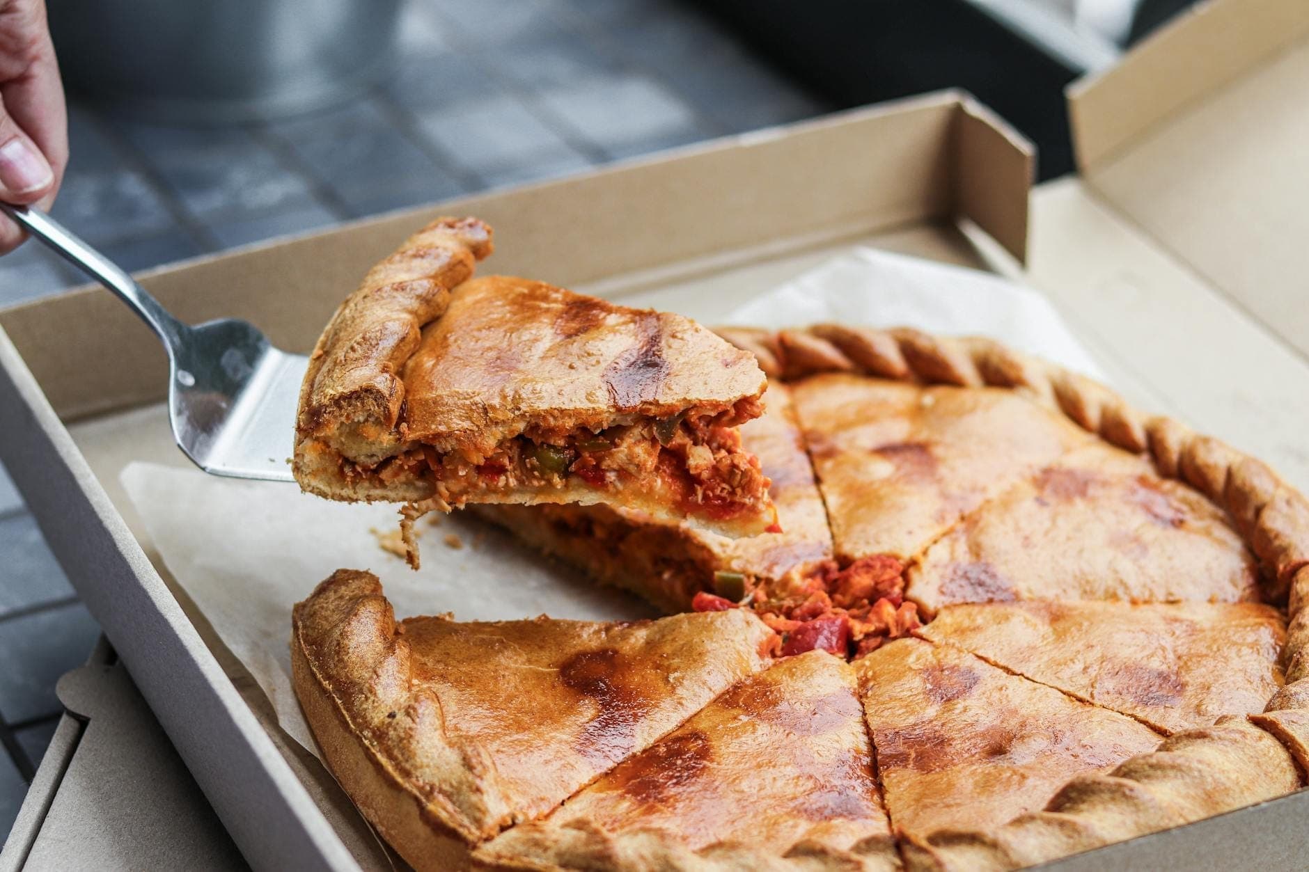 A Chicago-style deep dish pizza in an open box, with a slice being lifted out to reveal the thick, layered filling.