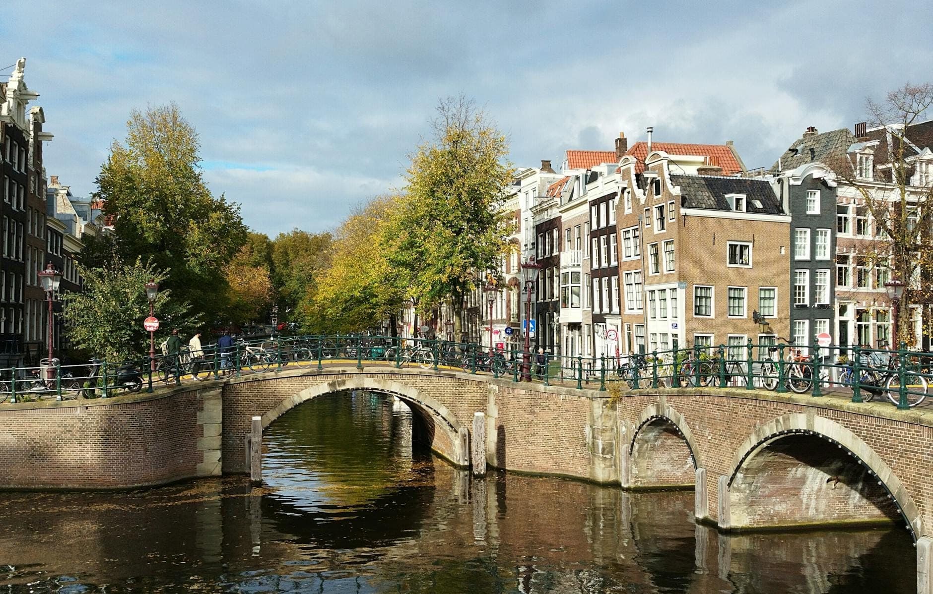 Klassische Kanalszene in Amsterdam mit Bogenbrücken, Fahrrädern und traditionellen schmalen Reihenhäusern am Wasser.