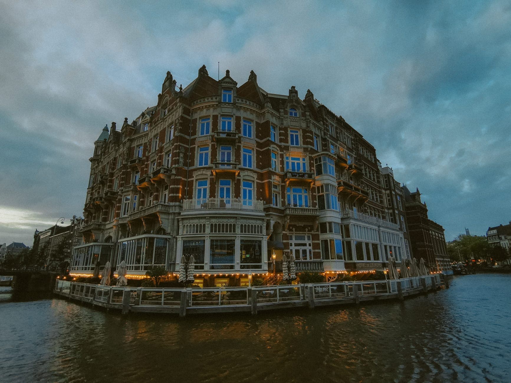 Historisches Grandhotel mit prachtvoller Fassade an einem Amsterdamer Gracht, in der Abenddämmerung beleuchtet und im Wasser gespiegelt.