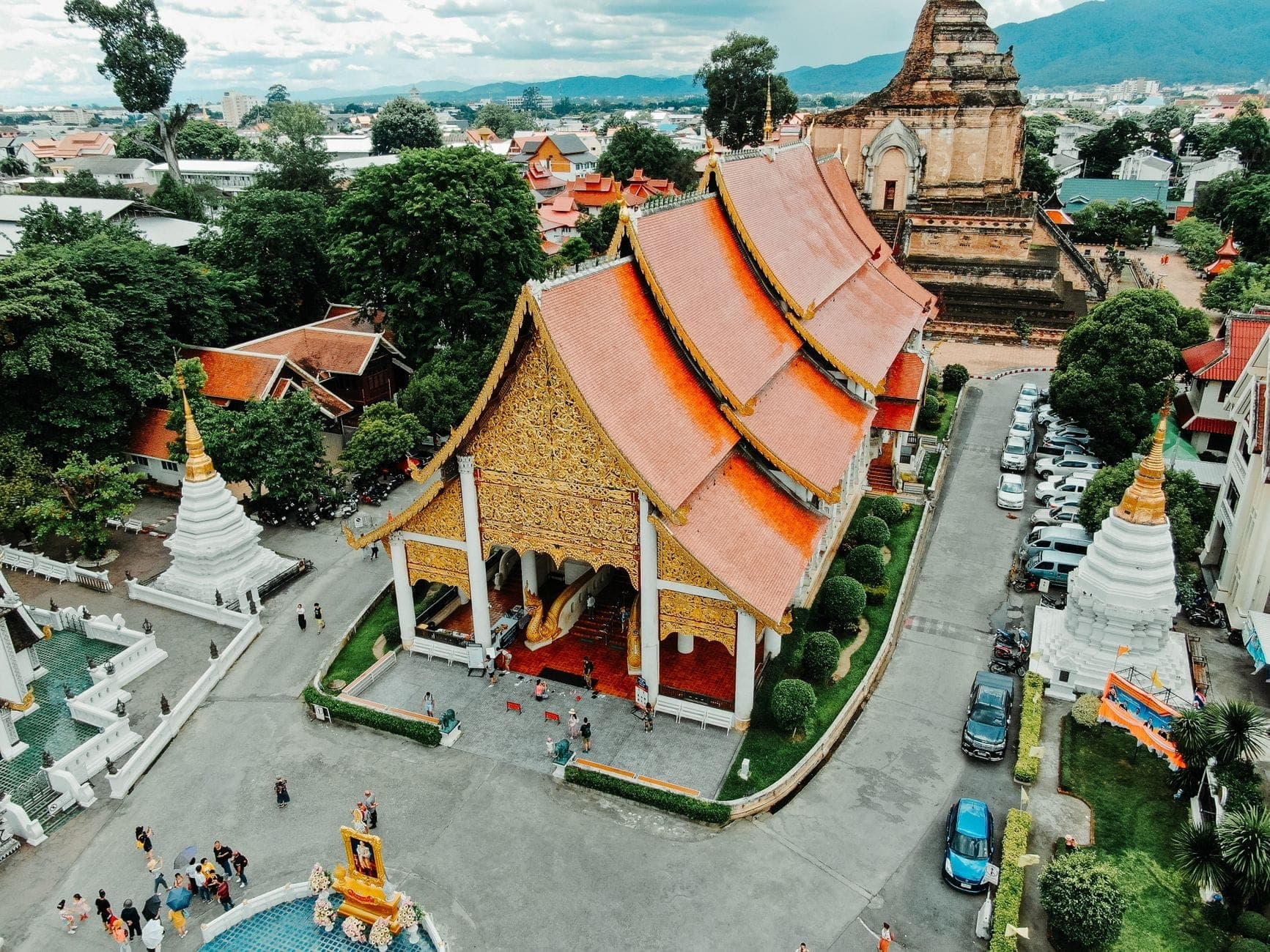 Luftaufnahme der Altstadt von Chiang Mai mit dem Tempel Wat Chedi Luang, historischen Dächern, umliegenden Straßen und Bergen im Hintergrund unter einem strahlend blauen Himmel.