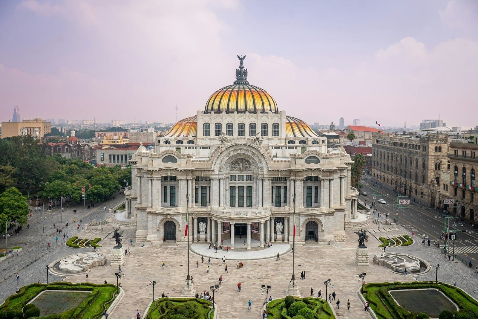 Aerial view of the Palacio de Bellas Artes in Mexico City's Centro Histórico, with gardens and historic buildings under a bright sky.