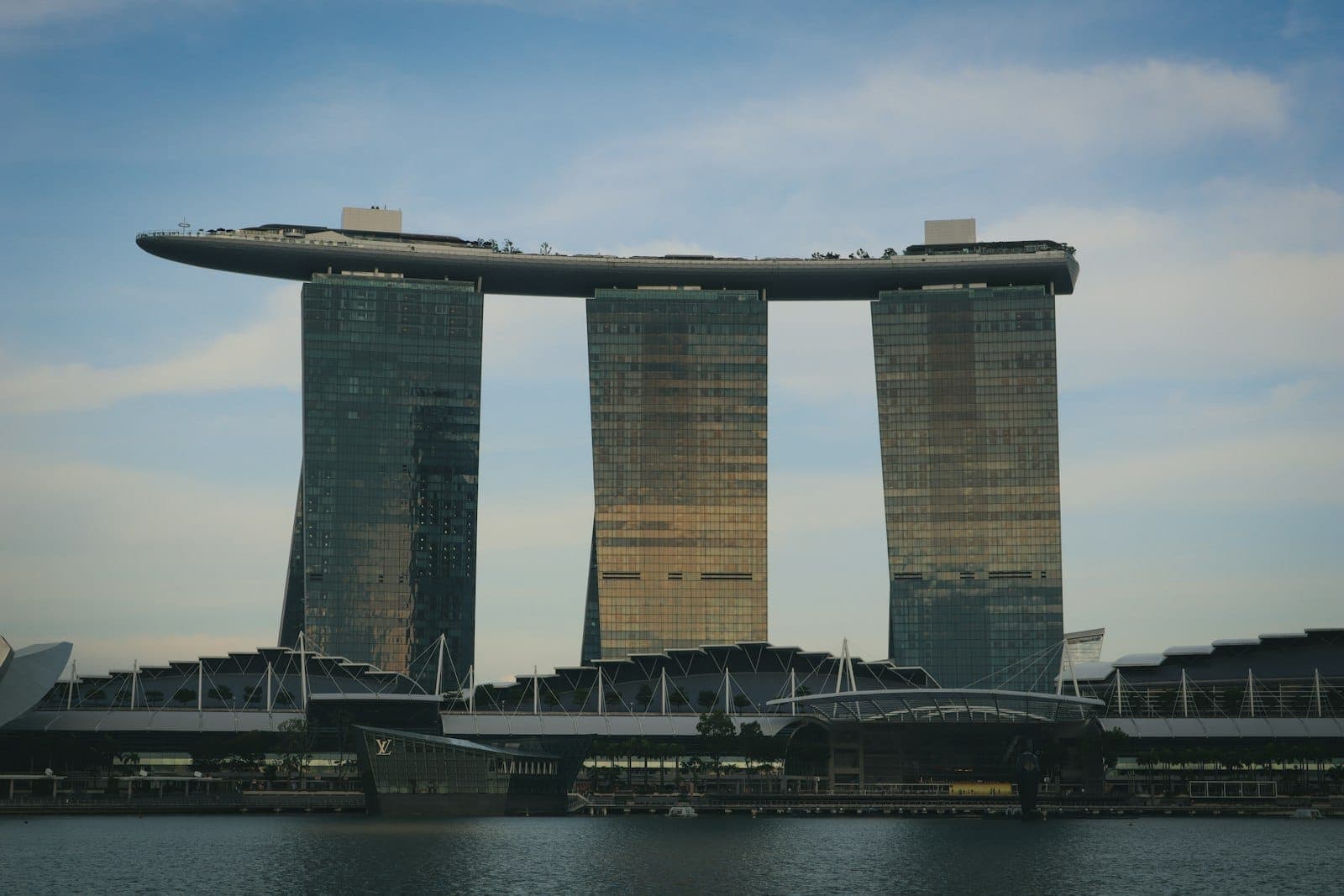 โรงแรม Marina Bay Sands พร้อมหอคอยสามแห่งและสวนลอยฟ้า มองเห็นในยามพลบค่ำข้ามอ่าวในสิงคโปร์