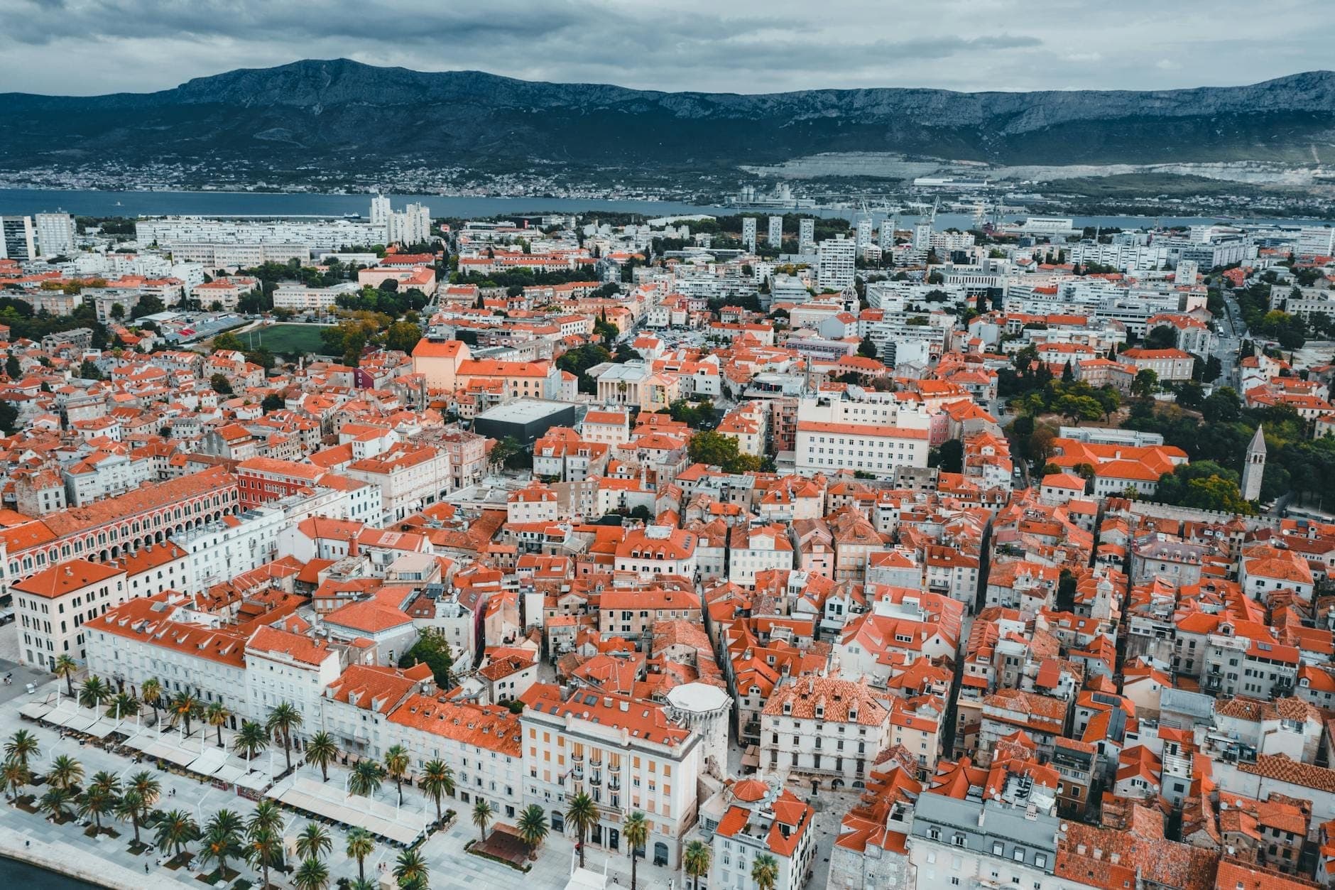 Vista aerea di Spalato, in Croazia, che mostra il compatto centro storico, gli edifici con tetti rossi, il lungomare centrale e i quartieri circostanti con le montagne sullo sfondo.