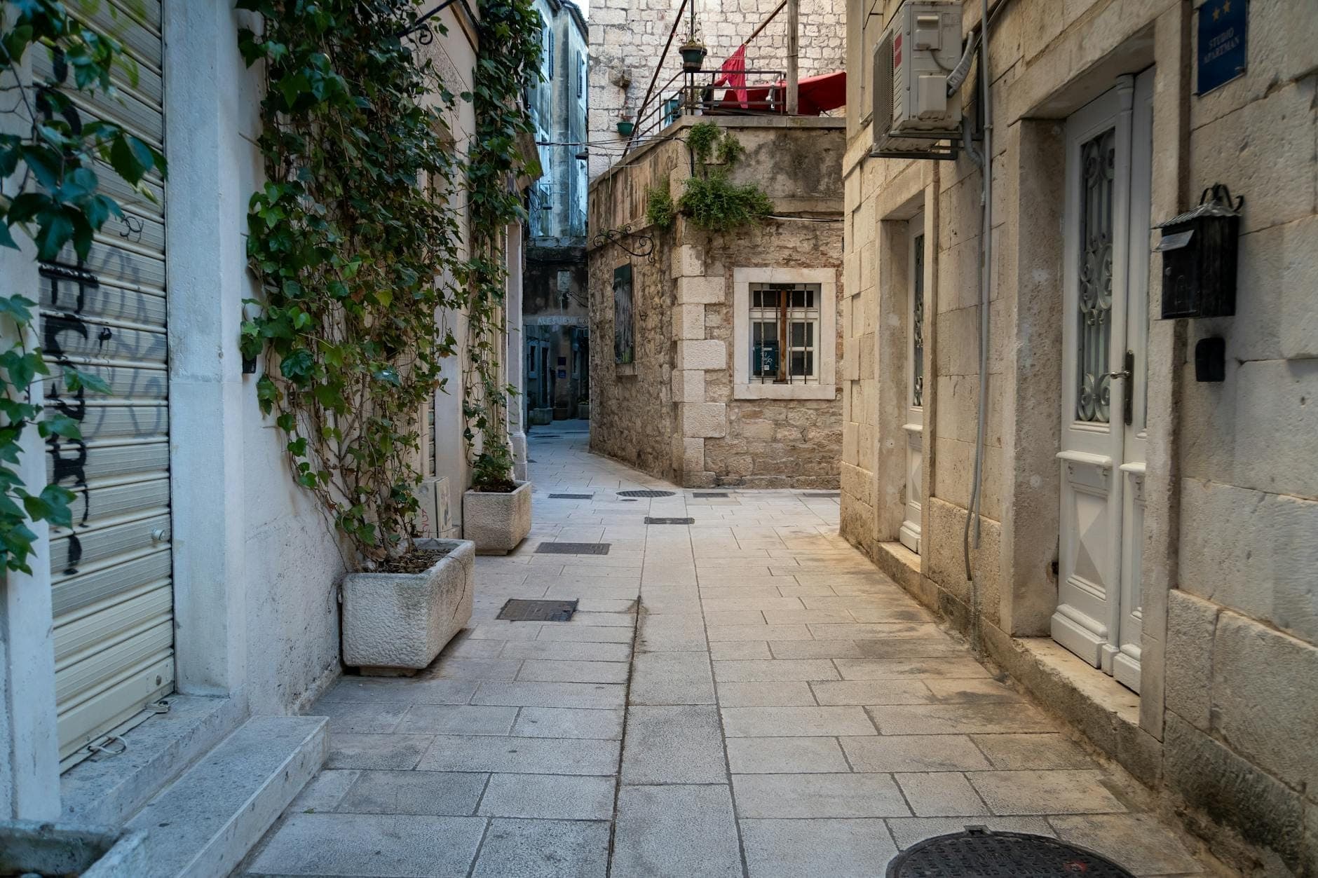 Stretto vicolo in pietra fiancheggiato da tradizionali case dalmate in pietra e persiane verdi in un antico quartiere di Spalato.