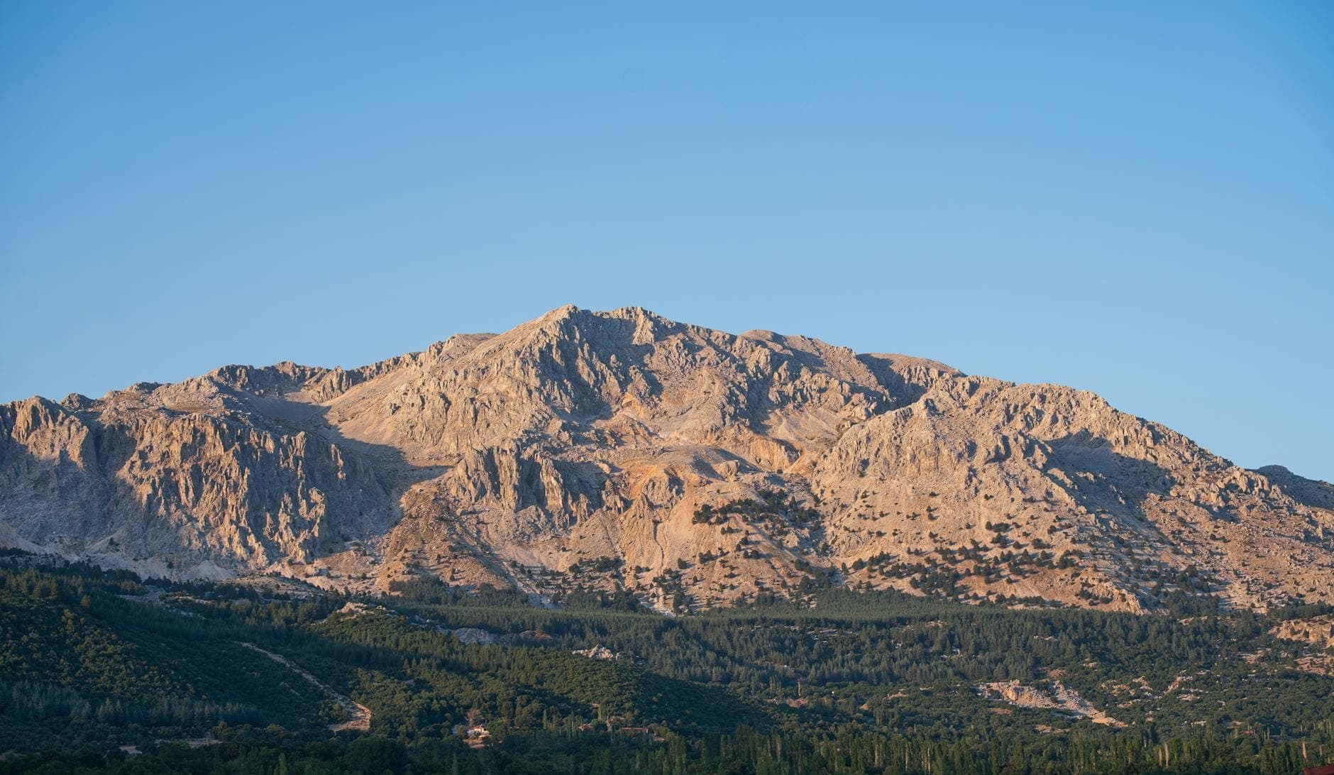 Weiter Blick auf die schroffen Kalksteingipfel der Weißen Berge (Lefka Ori) über dichten Wäldern unter einem klaren blauen Himmel auf Kreta.
