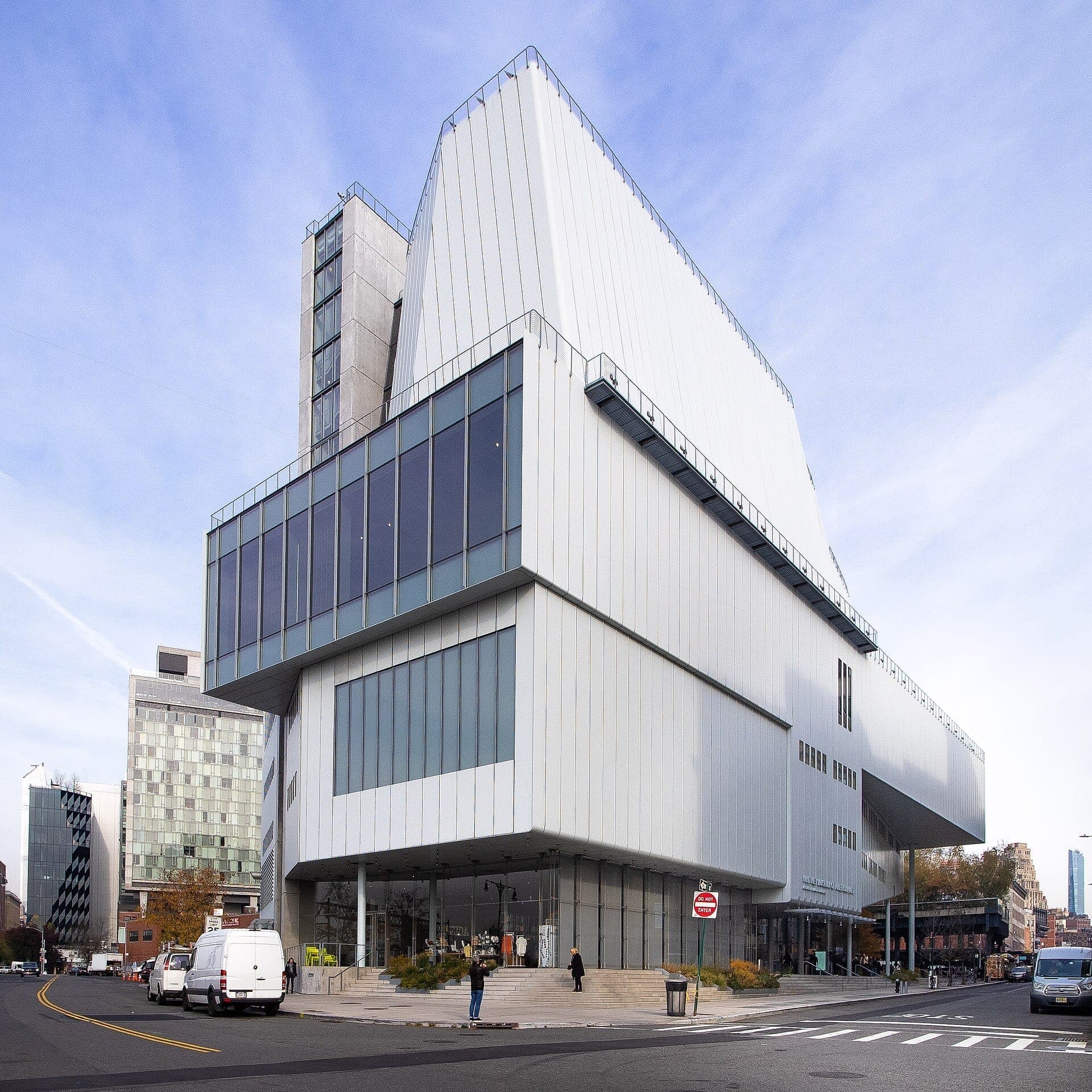ด้านนอกอาคารสมัยใหม่อันโดดเด่นของ Whitney Museum of American Art ประดับด้วยแผงกระจกและโลหะ ตั้งตระหง่านอยู่บนถนนในเมืองใต้ท้องฟ้าสีฟ้าใส