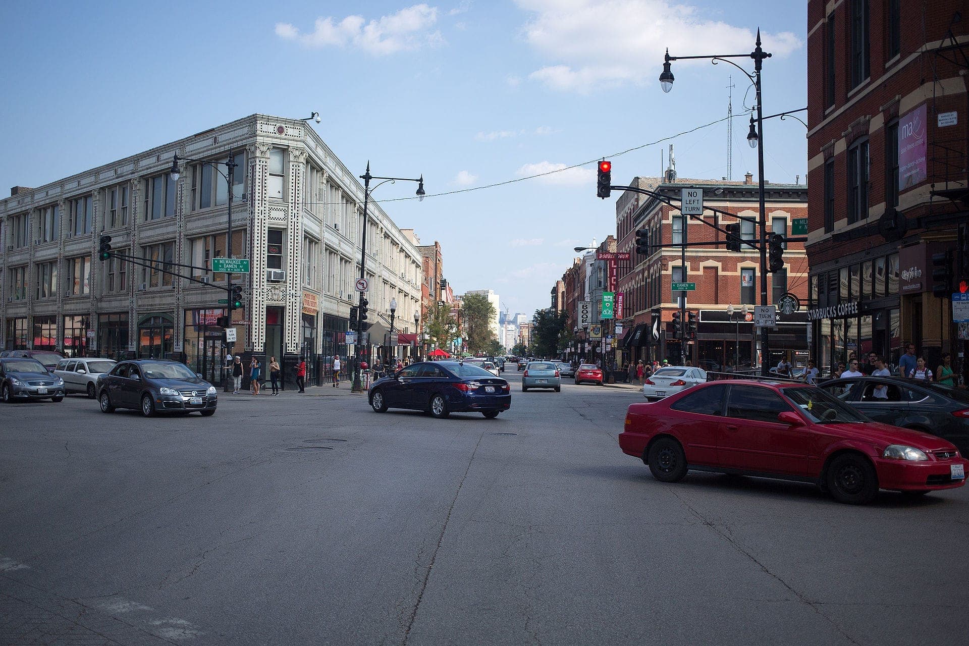Busy intersection in Wicker Park, Chicago, with historic greystone buildings, street signs, cars, pedestrians, and a Starbucks on a sunny day.