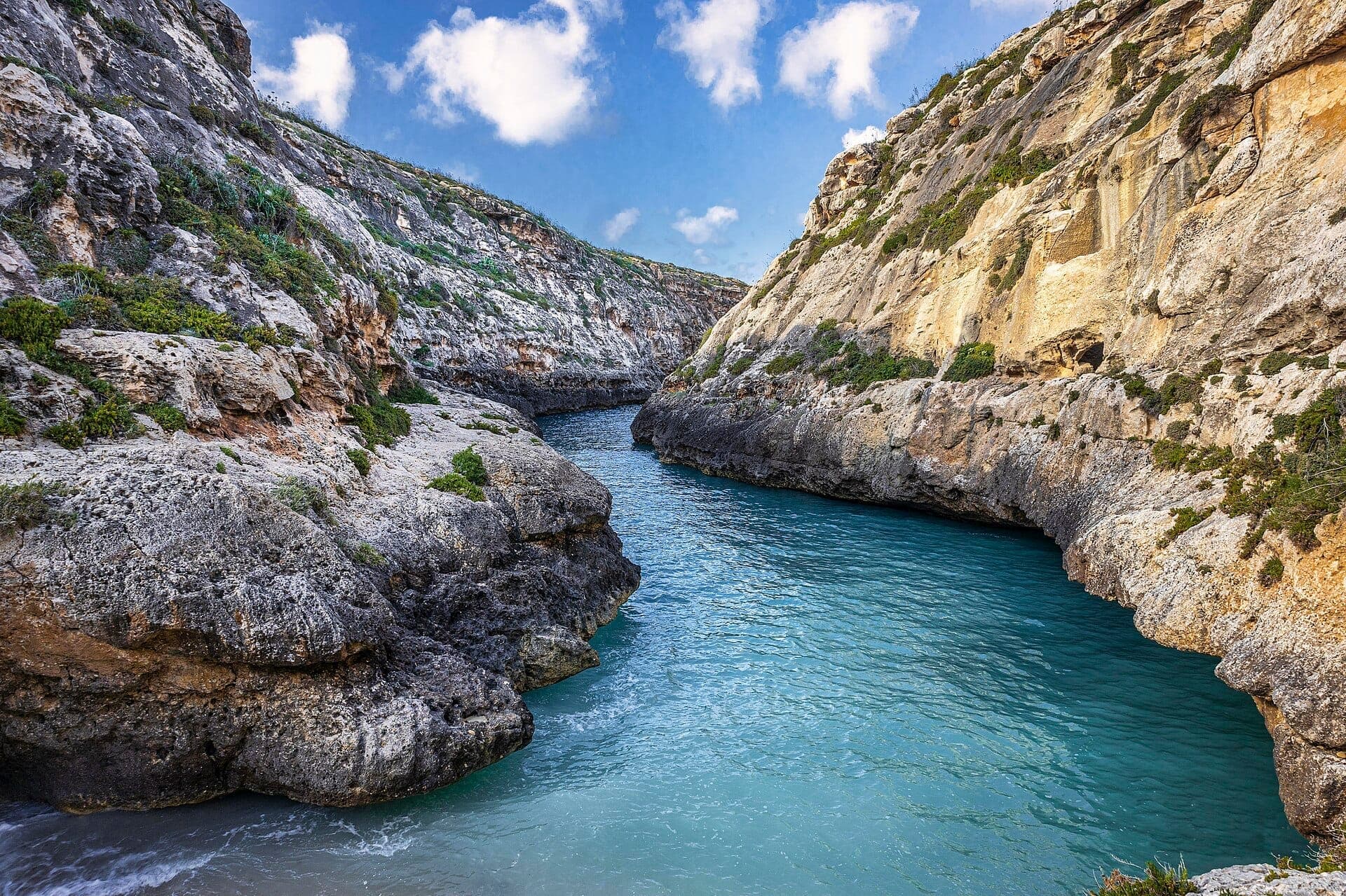 Die Schlucht Wied il-Għasri mit türkisfarbenem Wasser, das zwischen zerklüfteten Kalksteinklippen unter einem hellen Himmel an der Nordküste von Gozo fließt.