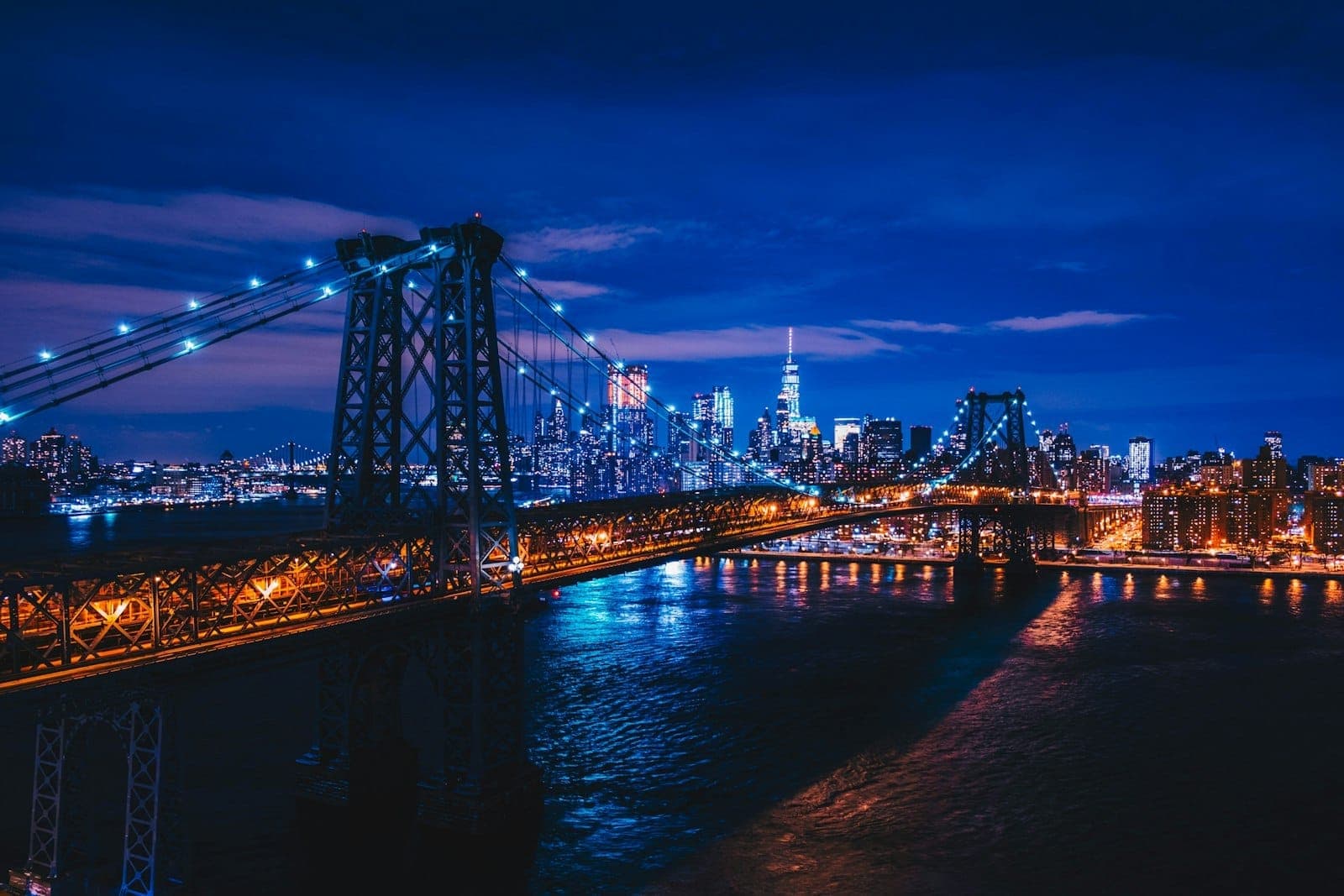 สะพาน Williamsburg ส่องไฟยามค่ำกับวิวตึกสูงของแมนฮัตตันฉากหลัง มองจากฝั่ง Brooklyn ข้ามแม่น้ำ East River