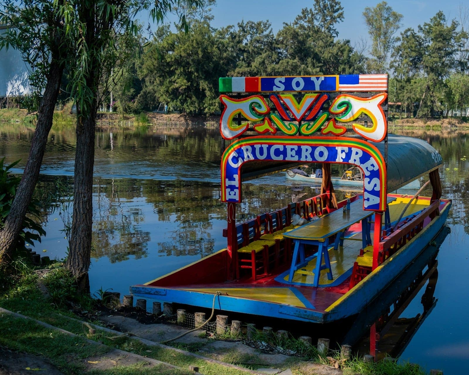 เรือทราชิเนราไม้สีสันสดใสตกแต่งลวดลายสไตล์ดั้งเดิมจอดอยู่ข้างคลองเงียบสงบ ล้อมรอบด้วยต้นไม้เขียวขจีในโซชิมิลโก