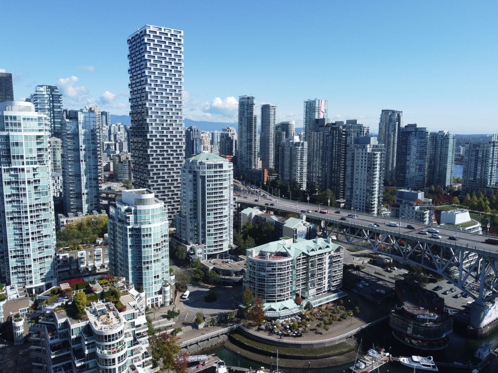 ภาพมุมสูงของ Yaletown ในเมือง Vancouver ที่มีคอนโดมิเนียมสูงสมัยใหม่ หอคอยกระจก และเรือจอดเทียบท่าตามแนวริมน้ำในวันที่แดดจ้า
