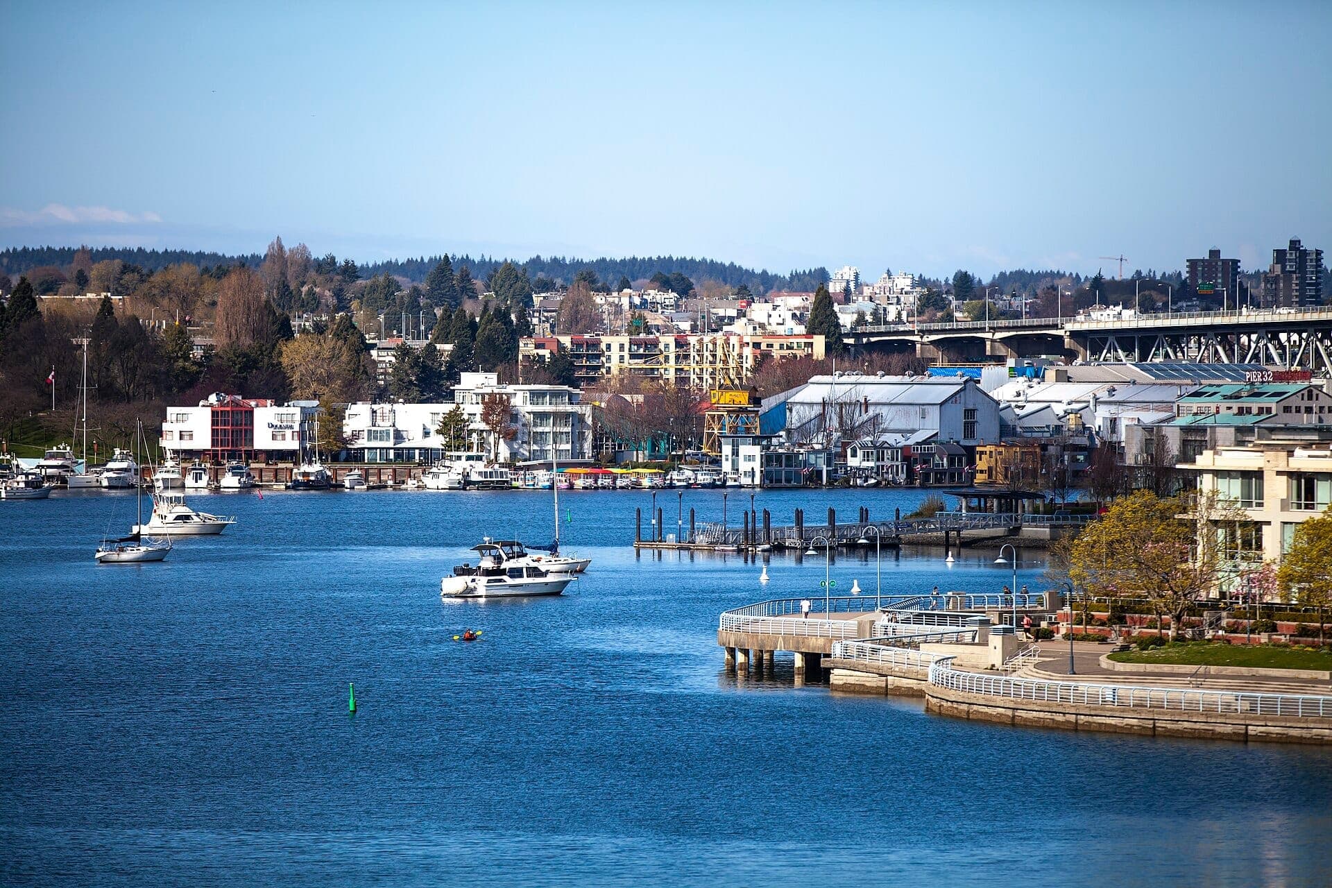 วิวของ False Creek และ Yaletown Seawall ในเมืองแวนคูเวอร์ โดดเด่นด้วยทางเดินริมน้ำ เรือบนผิวน้ำ และอาคารสมัยใหม่ภายใต้ท้องฟ้าสีฟ้าใส