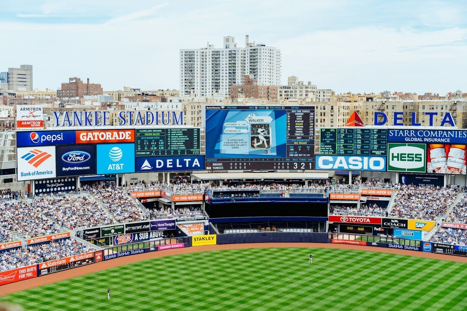 ภาพกว้างของสนาม Yankee Stadium อัฒจันทร์แน่นแฟนบอล เห็นสนาม, ป้ายคะแนน และตึกแถบเดอะบรองซ์ในวันที่แข่งสดใส
