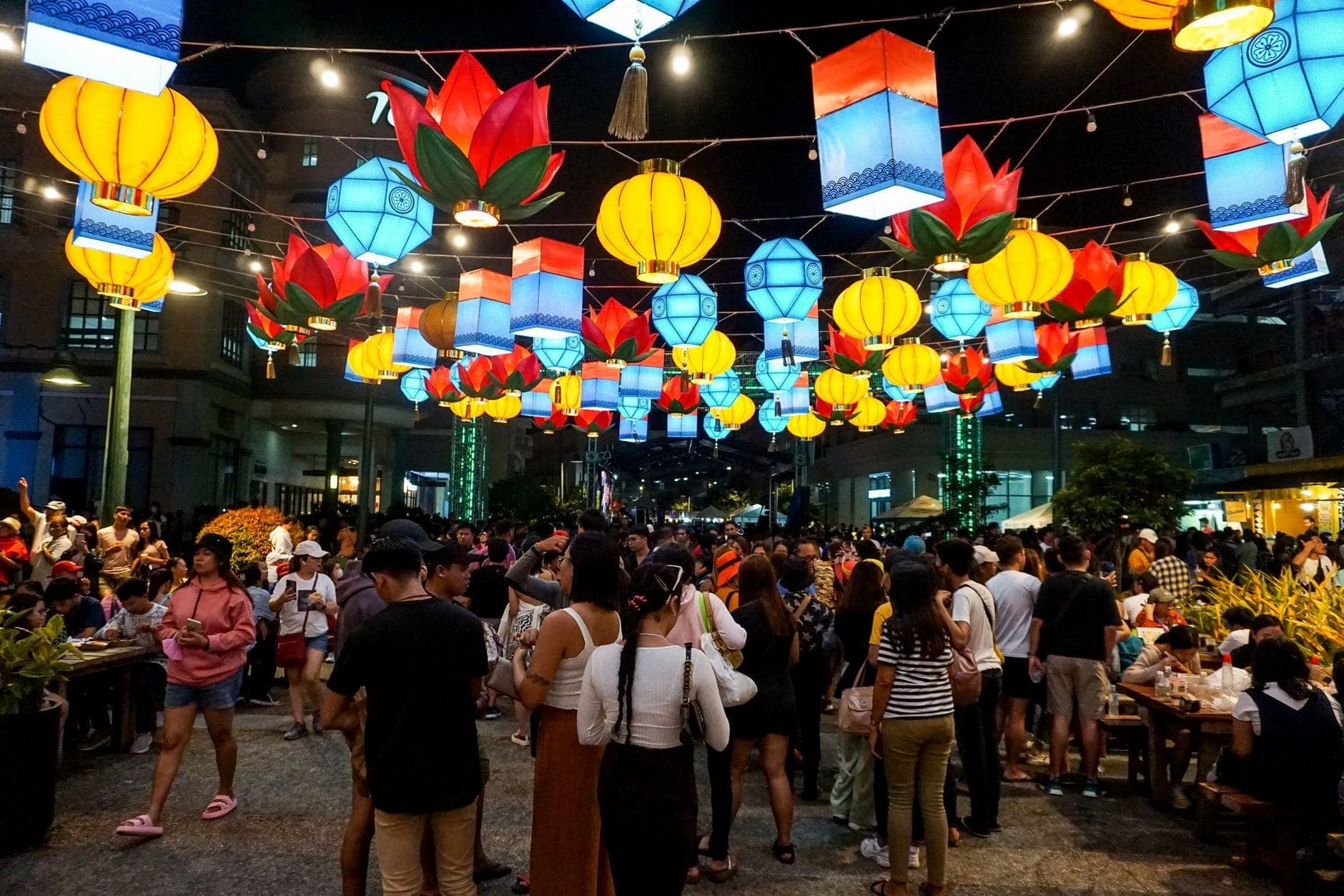 Calle concurrida en Chiang Mai de noche, decorada con coloridas linternas colgantes y llena de gente durante un festival.