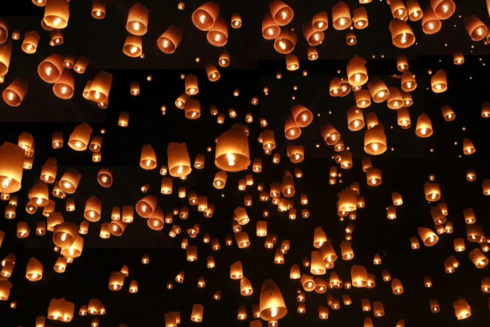 Cientos de linternas voladoras luminosas elevándose hacia el cielo nocturno durante un festival de linternas en Chiang Mai, Tailandia.