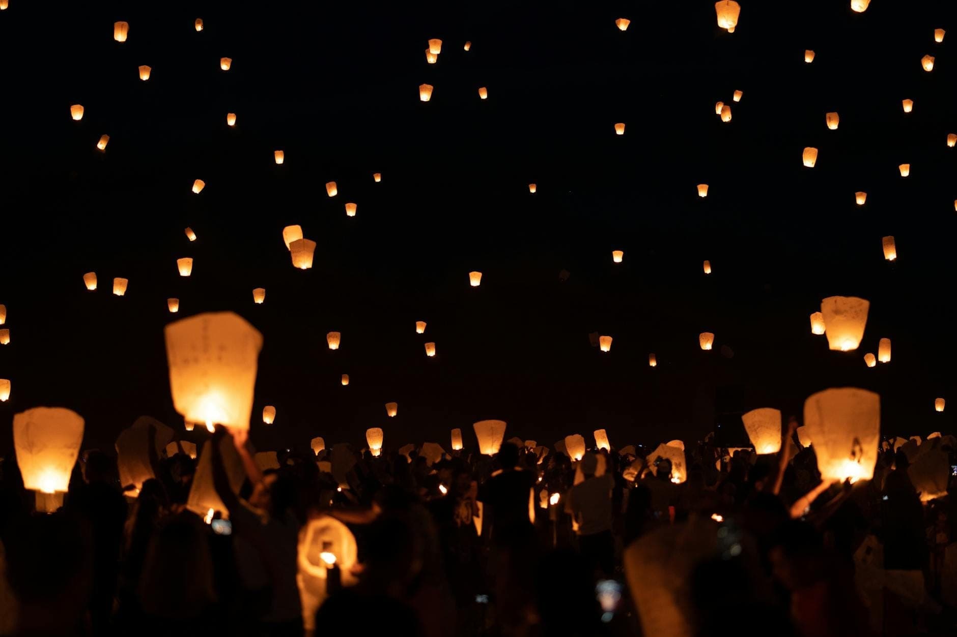 Escena nocturna de cientos de personas lanzando faroles luminosos al cielo en un festival masivo de linternas.