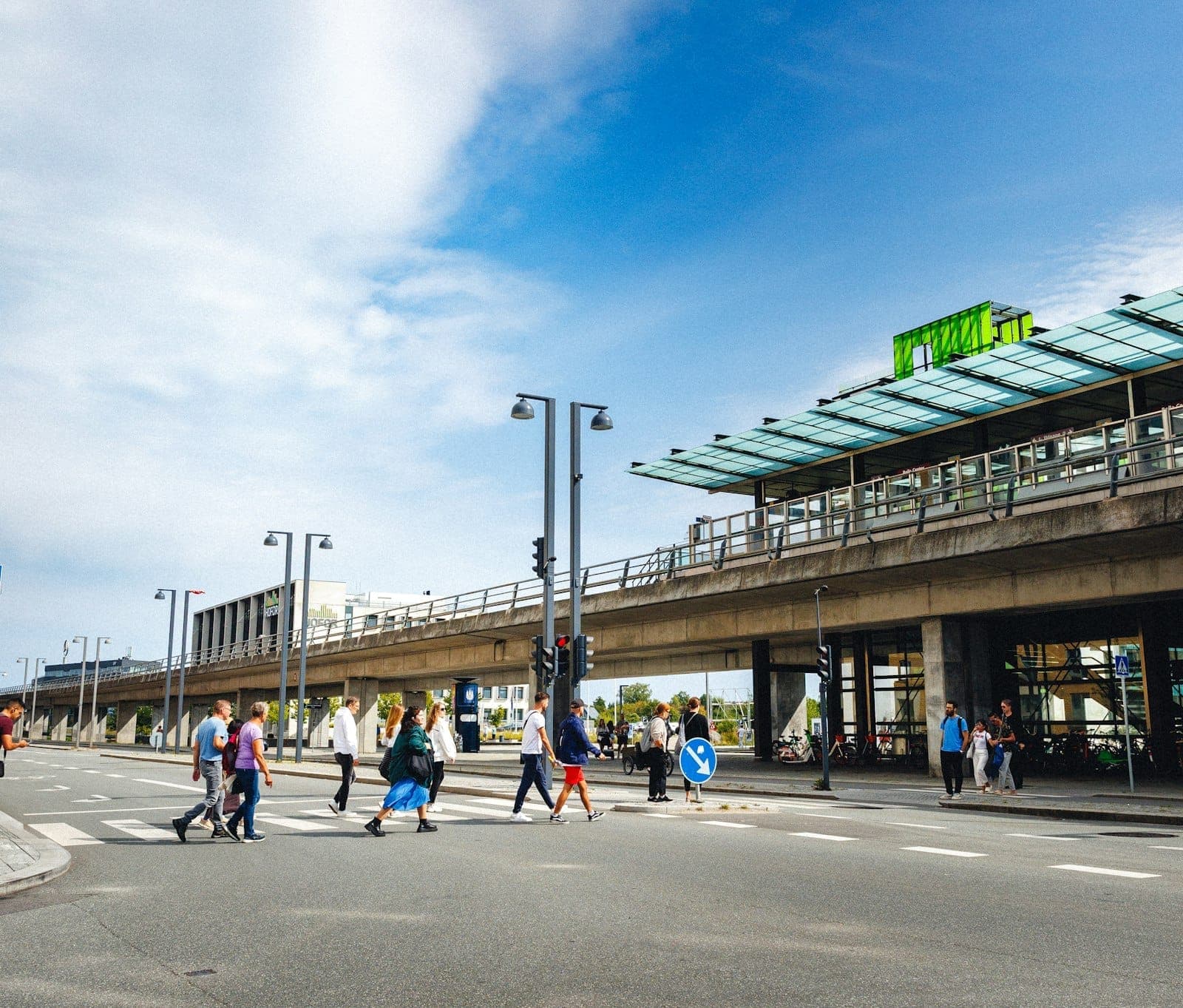 Viajantes atravessando a rua em frente ao aeroporto de Copenhague com o terminal visível sob um céu claro