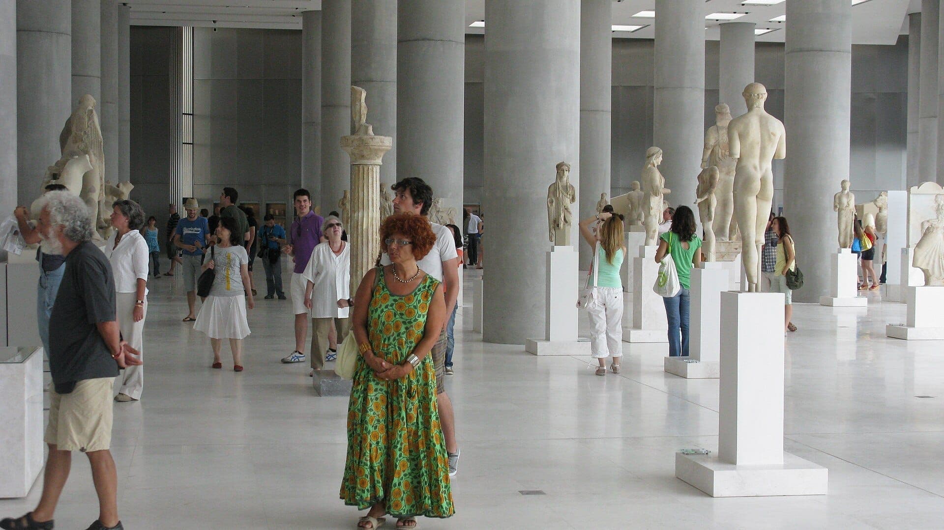 Visitors walk among ancient Greek statues in the bright, spacious main gallery of the Acropolis Museum in Athens.