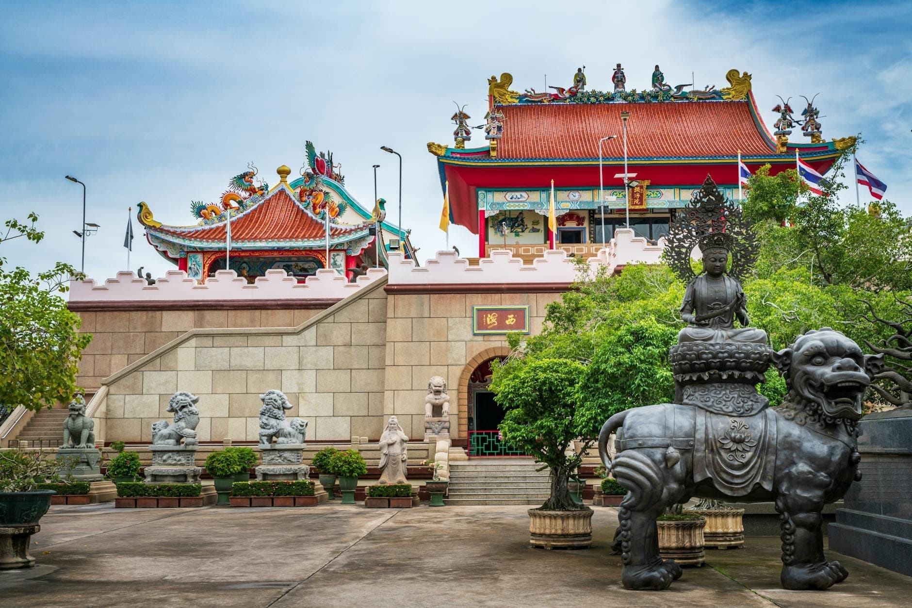 Entrance courtyard of Anek Kusala Sala with Chinese statues, intricate art sculptures, and colorful temple buildings under a bright sky in Pattaya, Thailand.