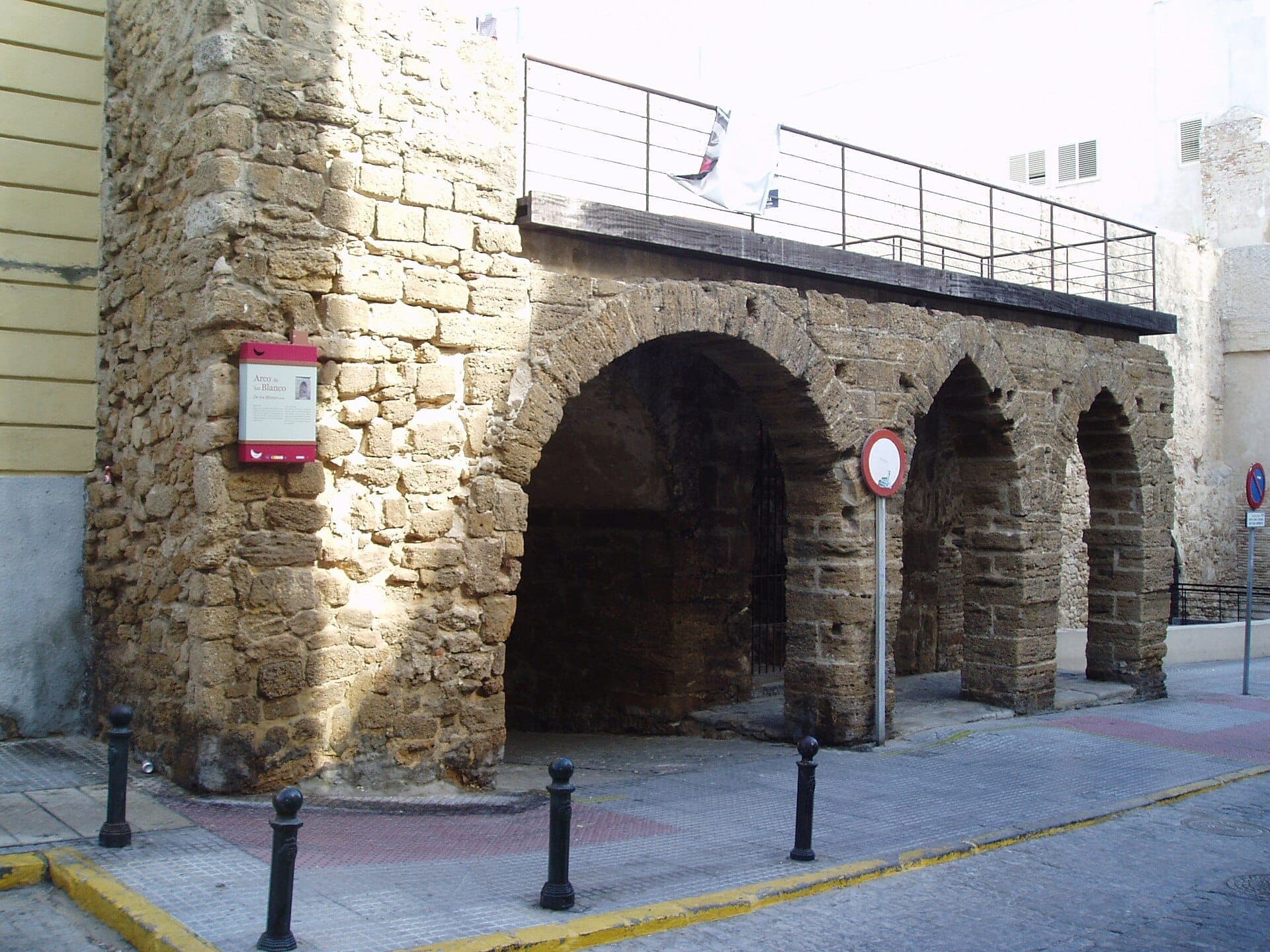 Những vòm đá của Arco del Pópulo, Cádiz, với những bức tường thời trung cổ mòn vẹt và biển báo đường phố hiện đại dưới ánh sáng ban ngày dịu nhẹ.
